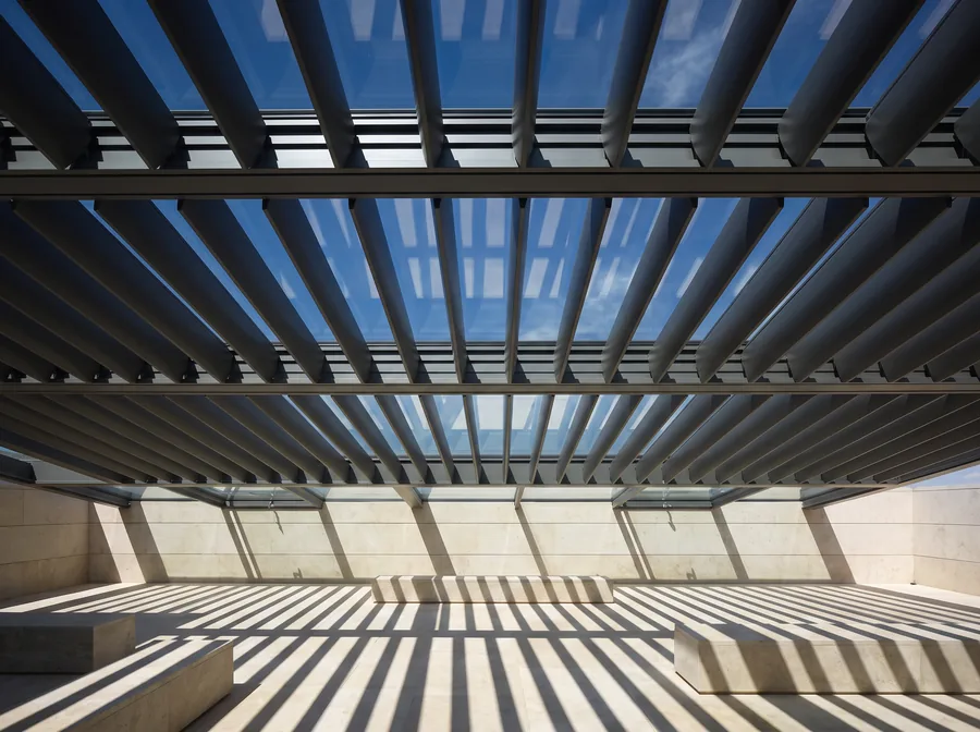 Blick von unten auf ein Glasdach mit drehbaren Aluminiumlamellen und Schattenstreifen