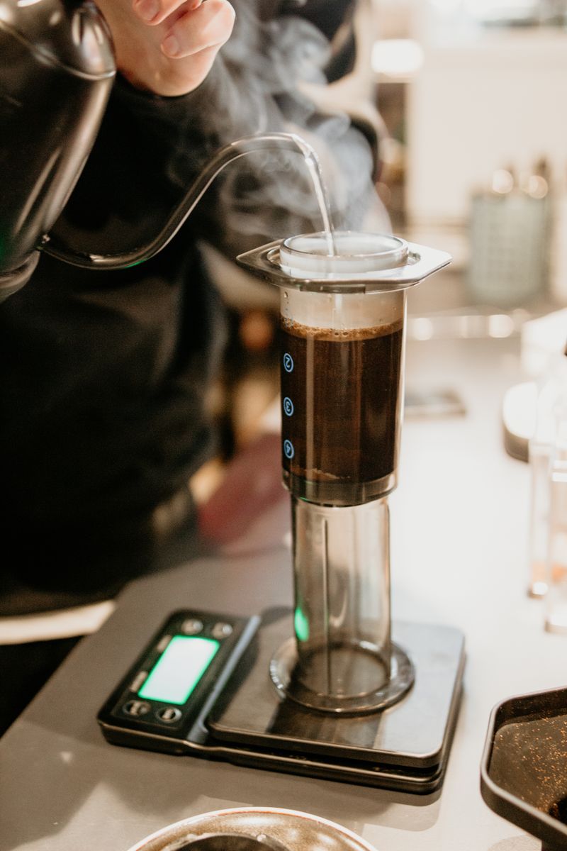 AeroPress auf der Barwaage, Dampf steigt über dem frisch aufgegossenen Kaffee auf.