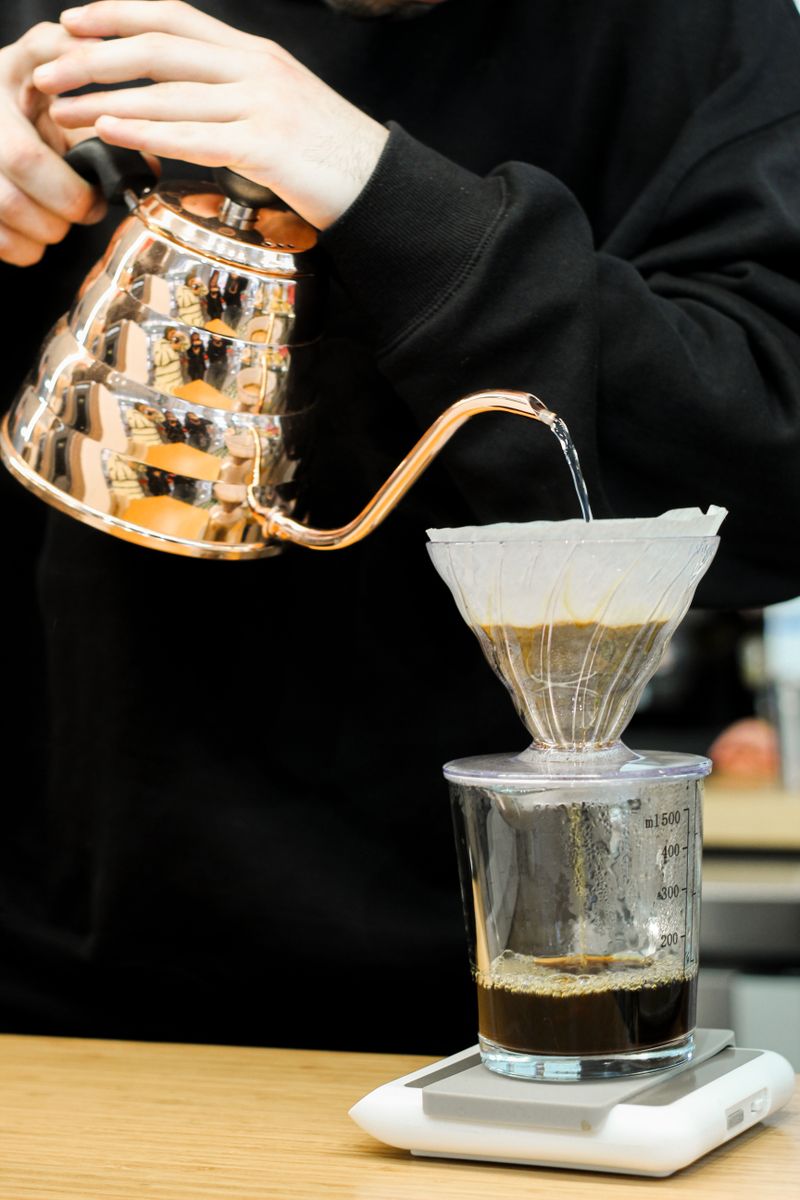 Barista gießt Kaffee aus einem kupfernen Schwanenhalskessel in einen Kegelfilter auf.