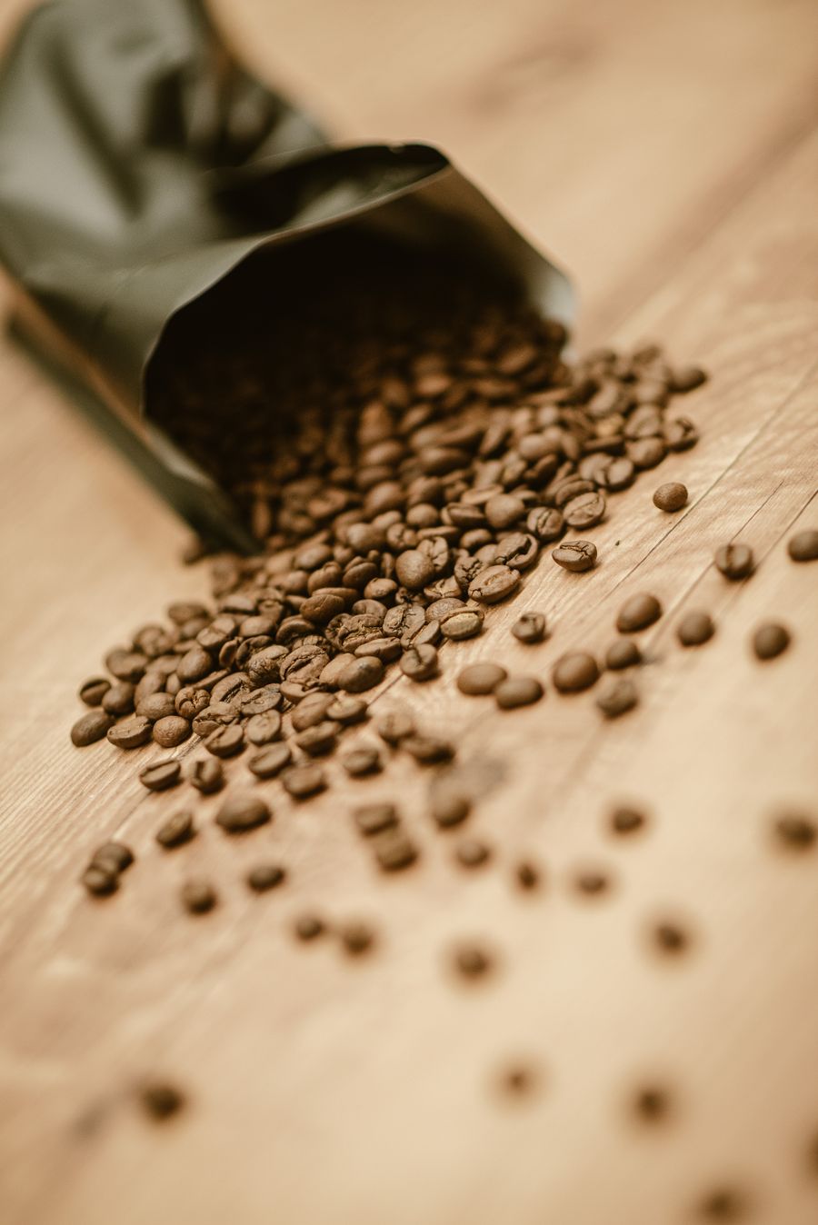 Matt schwarze Kaffeetüte, aus der Bohnen auf eine Holzplatte rollen.