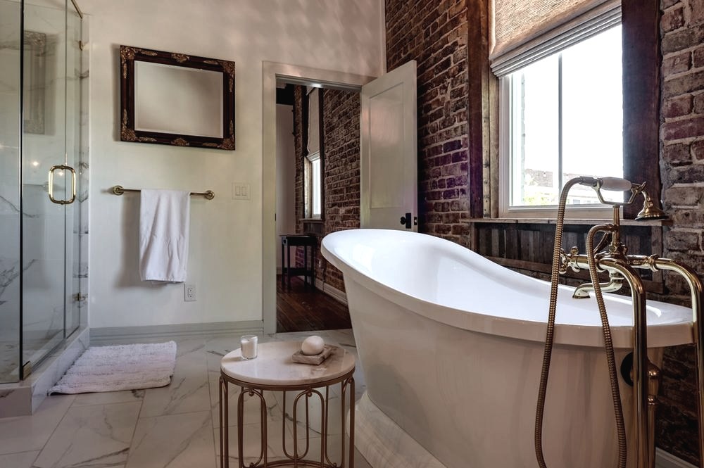 Badezimmer mit freistehender Wanne vor einer Ziegelwand und hohem Fenster